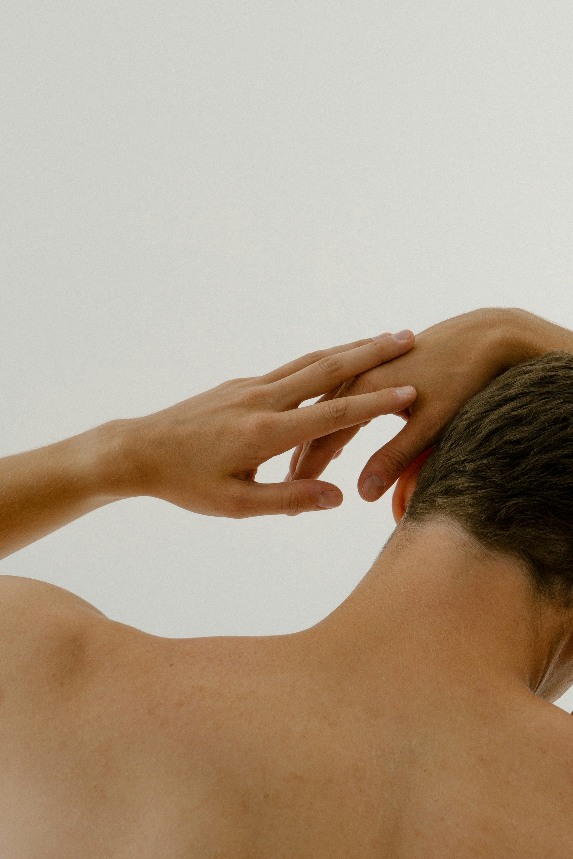 Bare back and neck of a person with one hand gently touching the back of their head.